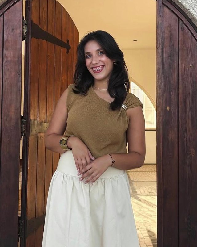 Portrait of Leonor Romana smiling, standing in a wooden arched doorway